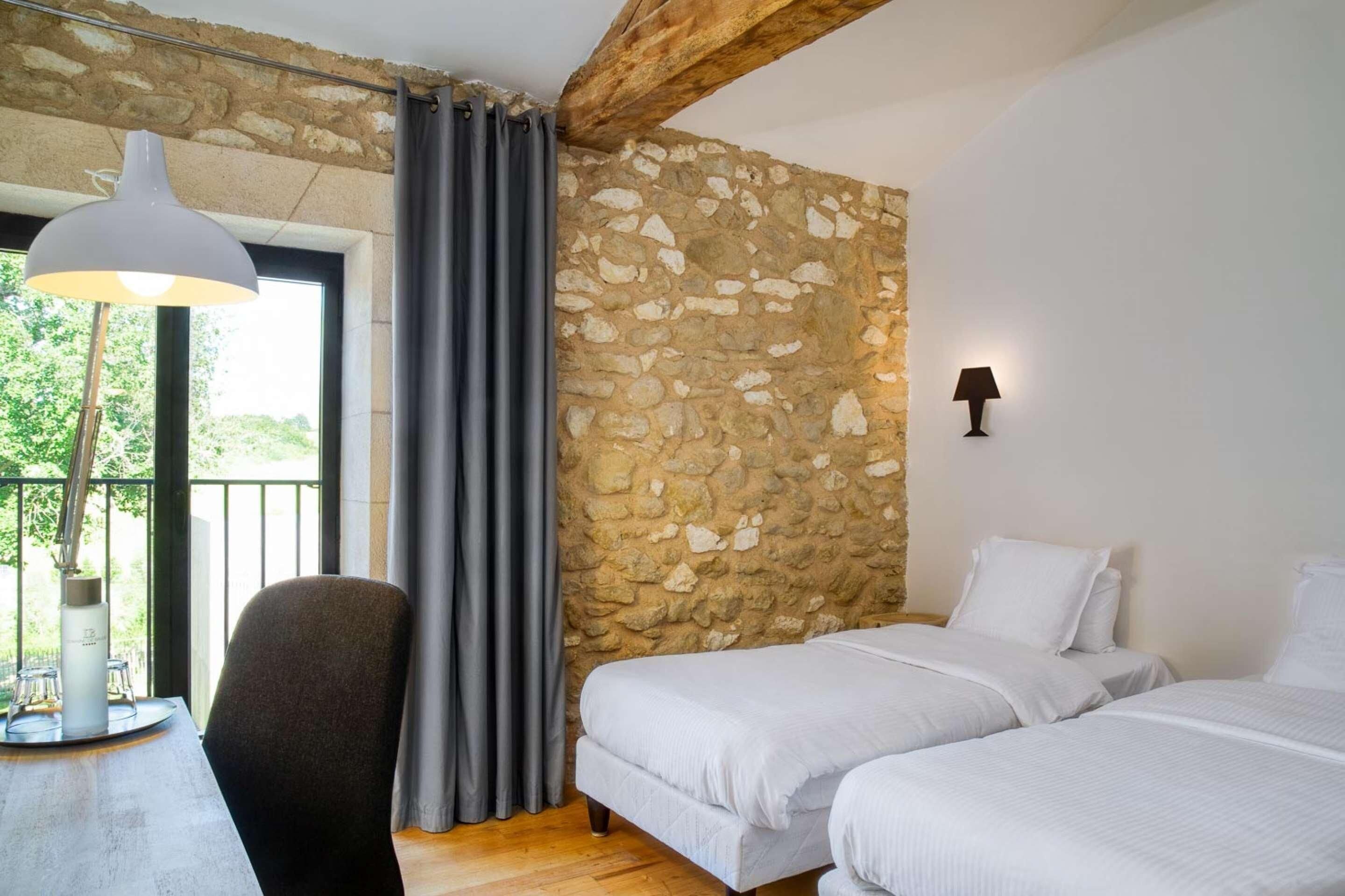 Un dormitorio con pared de piedra, dos camas, un escritorio con silla y una ventana con cortinas.