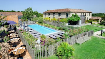 Un área junto a la piscina con una terraza de madera, sillas reclinables y un edificio de piedra al fondo.