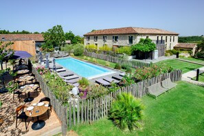 Un área junto a la piscina con una terraza de madera, sillas reclinables y un edificio de piedra al fondo.