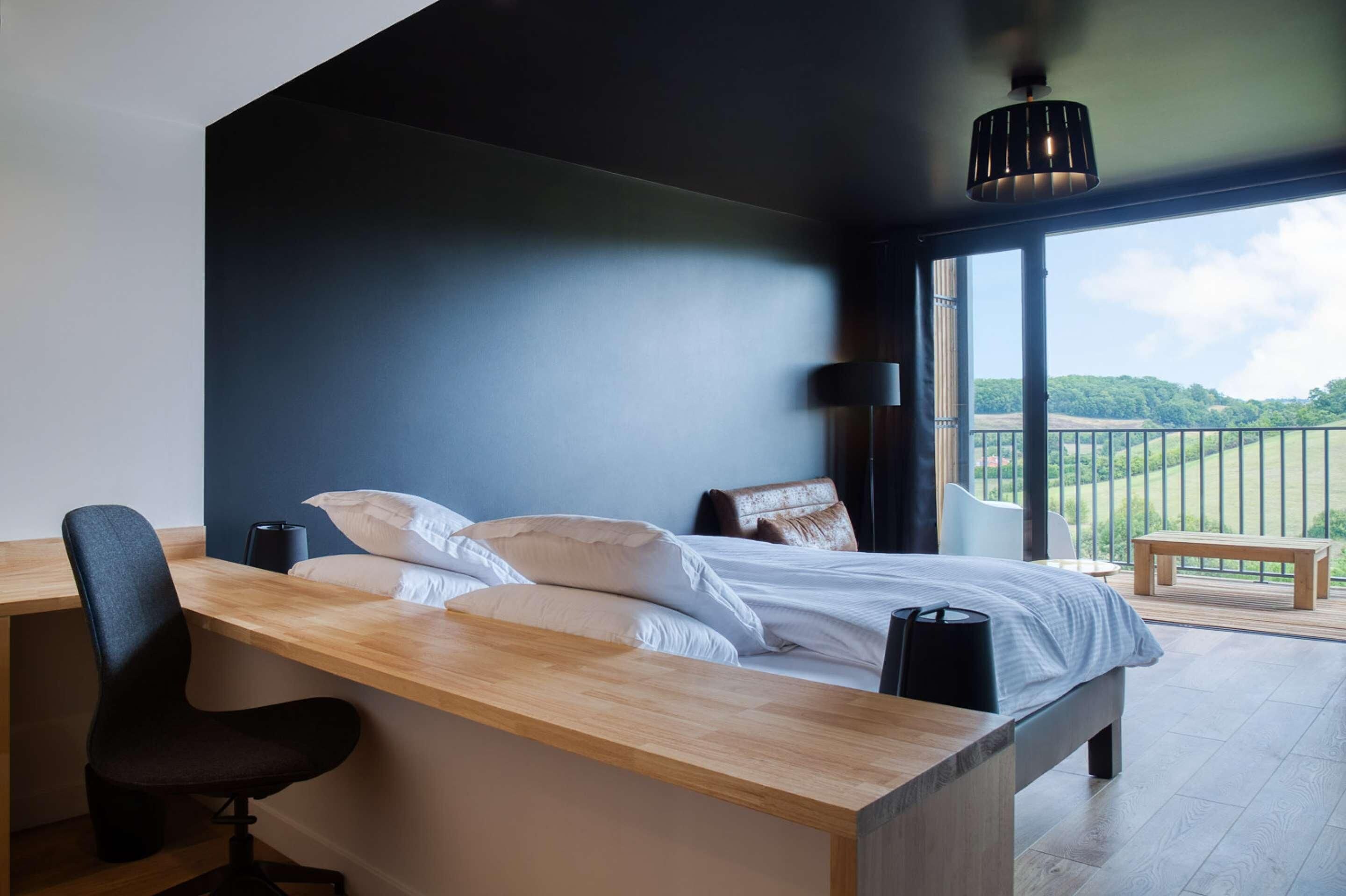 Ein modernes Schlafzimmer mit Bett, Schreibtisch, Stuhl und einem Balkon mit Blick.