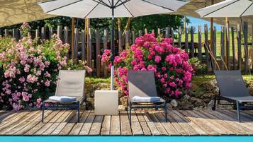 A poolside area with lounge chairs and umbrellas, surrounded by flowering bushes.