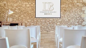 Interior de una pared de piedra con sillas blancas dispuestas para sentarse, un letrero enmarcado con el texto 'DB DOMAINE DE BAULIEU' y una mesa con una lámpara.