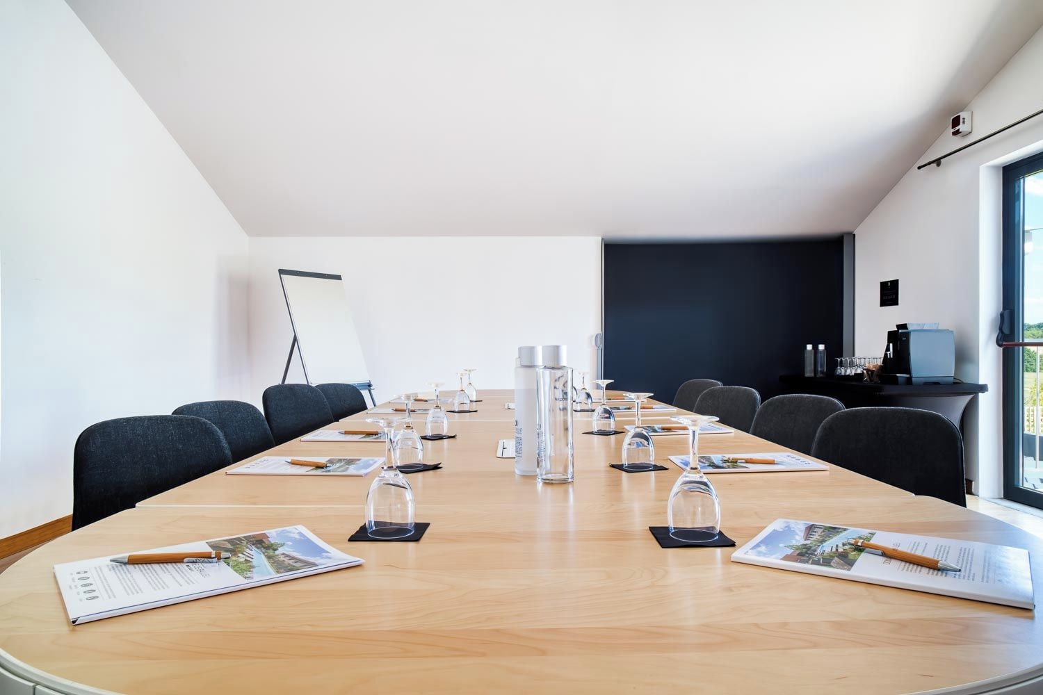 Un salón de conferencias con una larga mesa, sillas y una pantalla de proyector.
