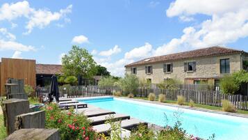 A swimming pool with lounge chairs, a stone building with windows, and a wooden fence.