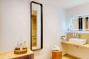 A modern bathroom with a large mirror, a sink, and toiletries on a wooden stand.