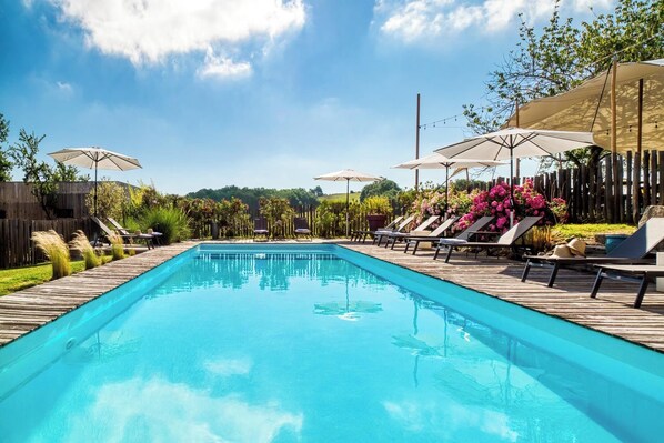 A rectangular swimming pool with lounge chairs and umbrellas on a wooden deck.