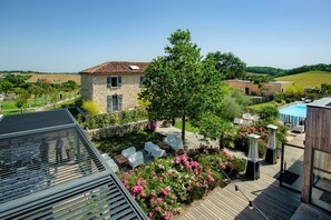 A rooftop terrace with outdoor seating, a swimming pool, and a stone building in the background. - Hotel Le Domaine De Baulieu (Auch)