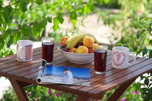 A wooden table with a bowl of fruit, two mugs, a glass of tea, and a magazine. - Studios Vrionis Panoramic Sunset (Kefalonia)