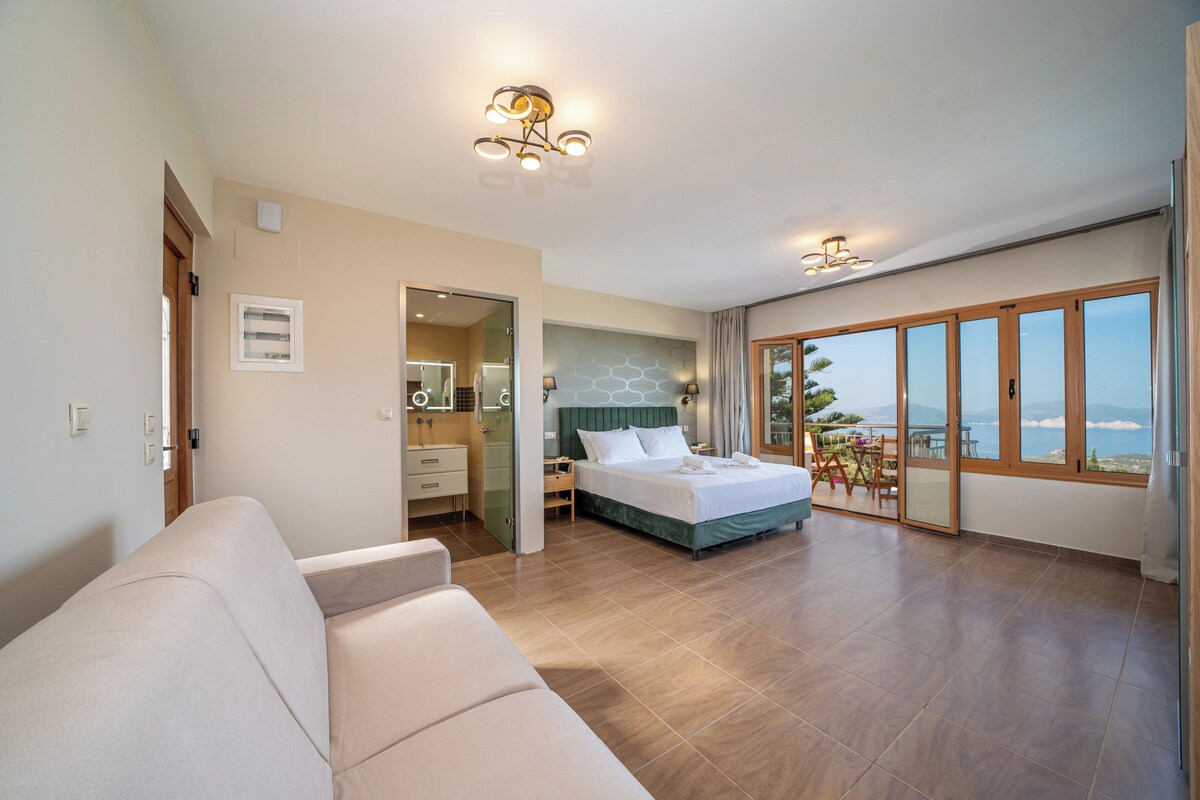 A modern hotel room with a large bed, a sofa, a bathroom, and a balcony with a view.
