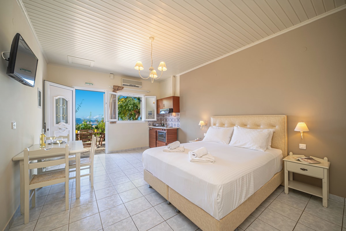 A bedroom with a large bed, a bedside table, a TV mounted on the wall, and a view of the outdoors.