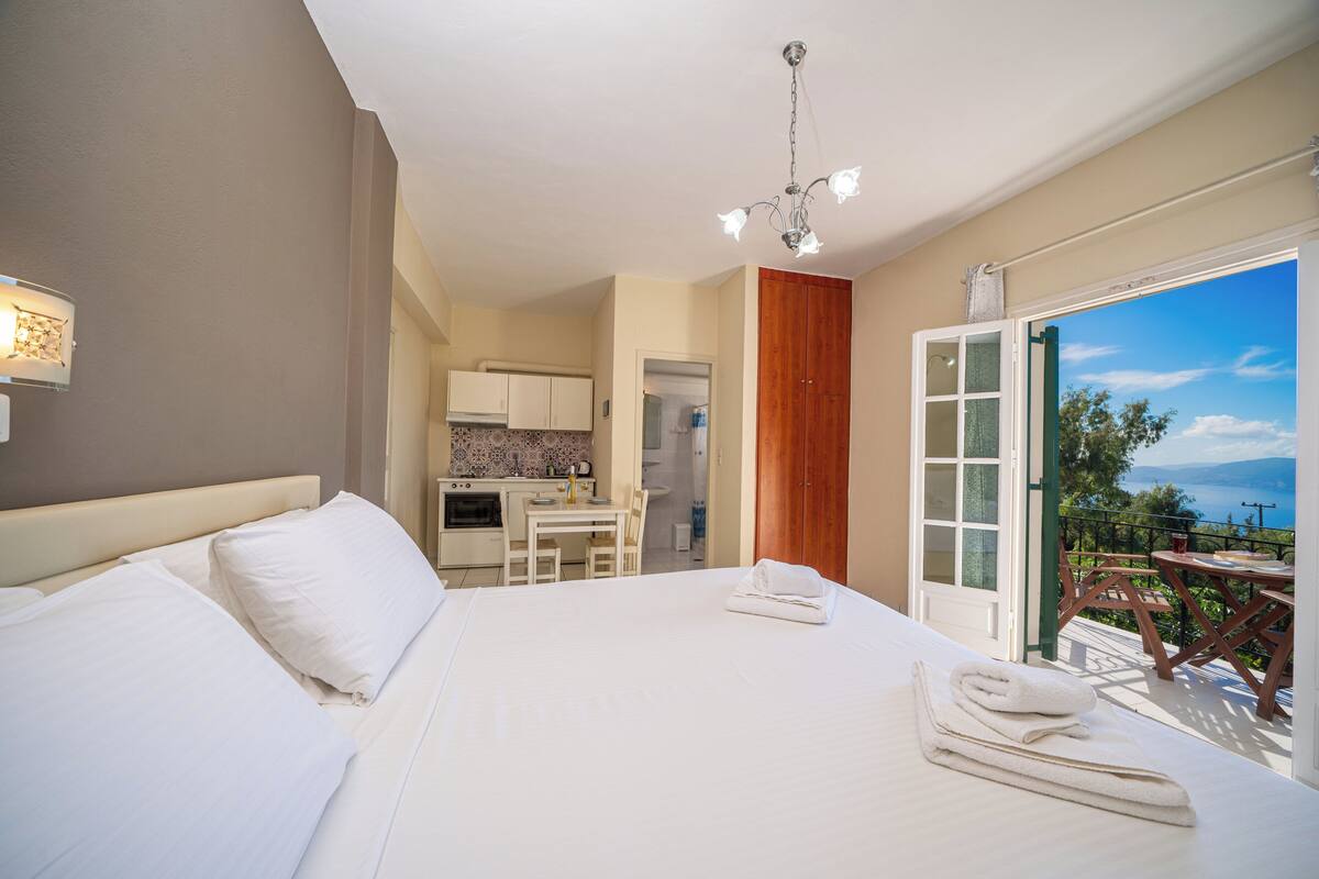 A hotel room with a large bed, a kitchenette, and a balcony with a view.