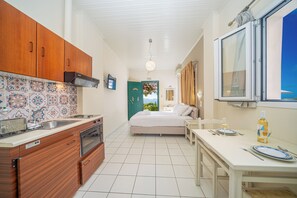 A compact kitchen with wooden cabinets, a tiled backsplash, and a dining area with a table set for two. - Studios Vrionis Panoramic Sunset (Kefalonia)