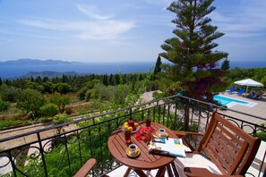A balcony with a table set for two, a chair, and a view of the sea and mountains. - Studios Vrionis Panoramic Sunset (Kefalonia)