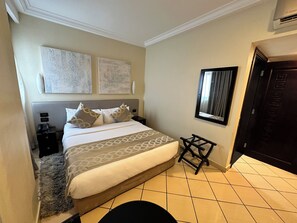 A hotel room with a bed, bedside tables, a small stool, a mirror, and artwork on the wall. - Oak Plaza Hotel East Airport (Accra)