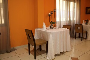 A dining area with a table set for two, chairs, a vase with a plant, and candles on the wall. - Oak Plaza Hotel East Airport (Accra)