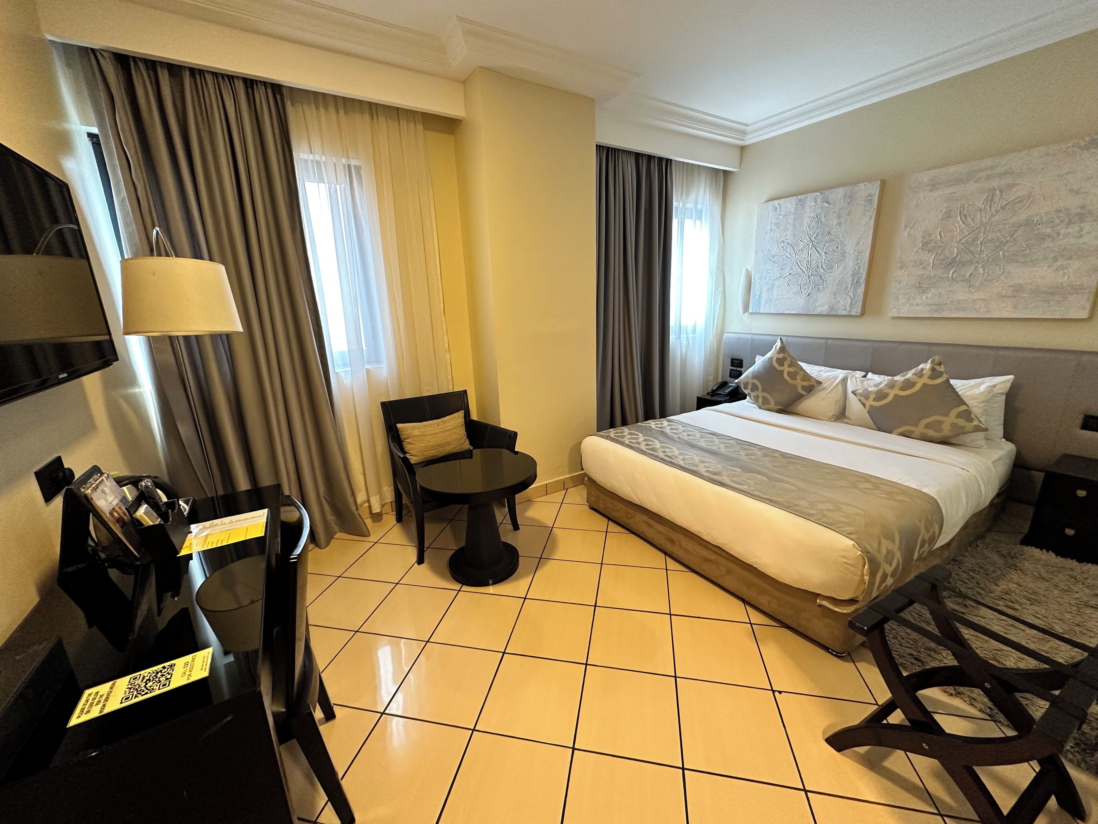 A hotel room with a bed, a chair, a small table, a TV, and a telephone.