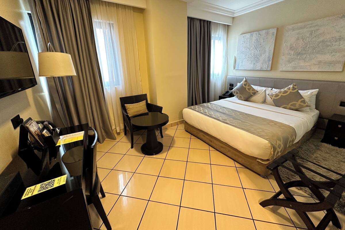 A hotel room with a bed, a chair, a small table, a TV, and a telephone.
