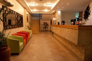 A hotel lobby with a reception desk, a staircase, and a row of colorful chairs. - Oak Plaza Hotel East Airport (Accra)