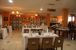 A dining area with tables set for service, a decorative plant centerpiece, and a large painting on the wall. - Oak Plaza Hotel East Airport (Accra)