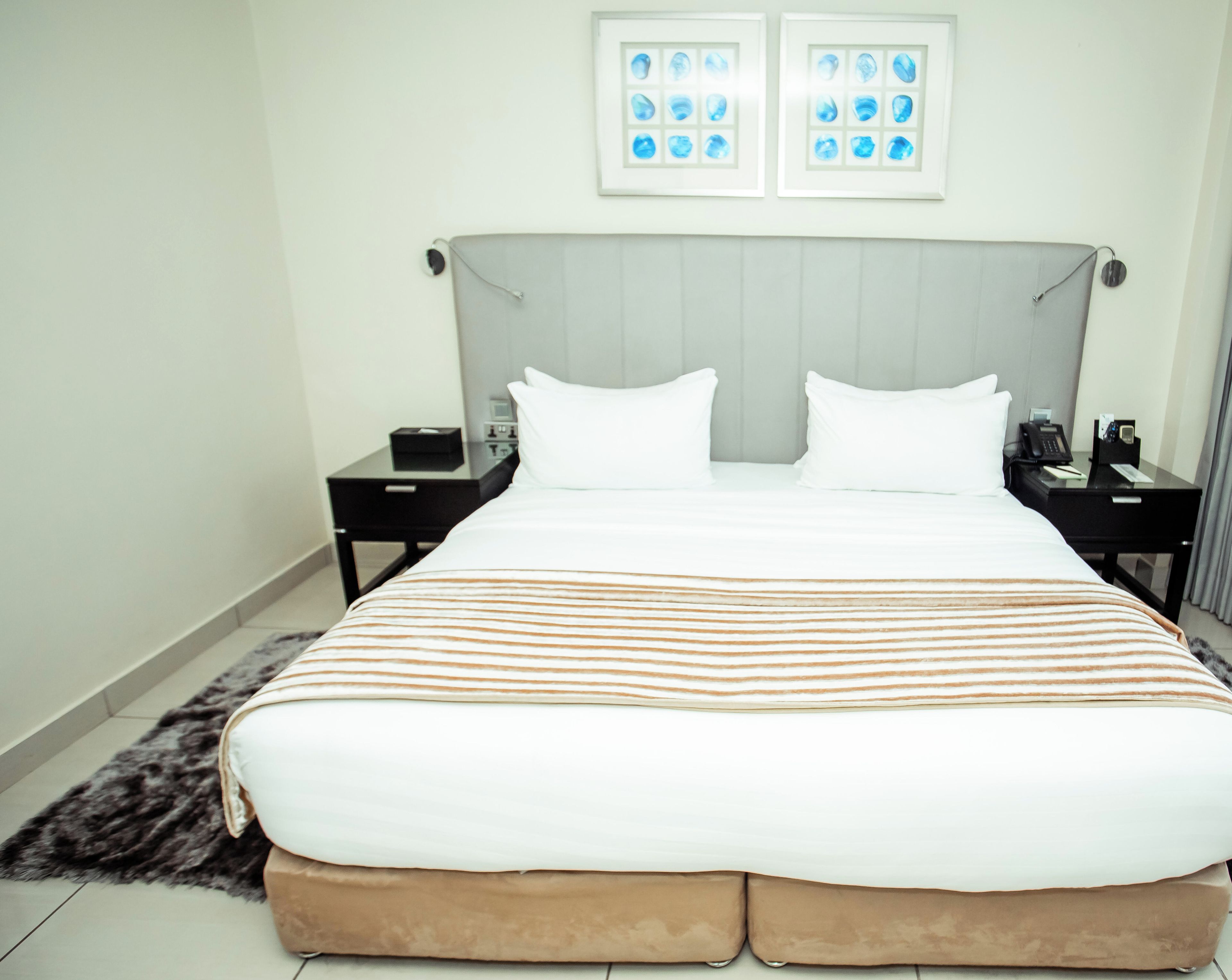 Een hotelkamer met een groot bed, twee nachtkastjes, een lamp en een lijst met een afbeelding boven het bed.