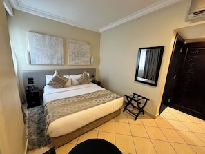 A hotel room with a bed, bedside tables, a small stool, a mirror, and artwork on the wall. - Oak Plaza Hotel East Airport (Accra)
