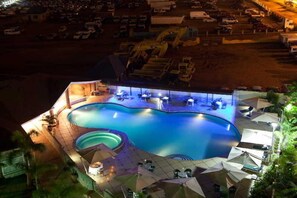 A swimming pool with a sunken area, surrounded by lounge chairs and umbrellas, with a view of the surrounding area. - Oak Plaza Hotel East Airport (Accra)
