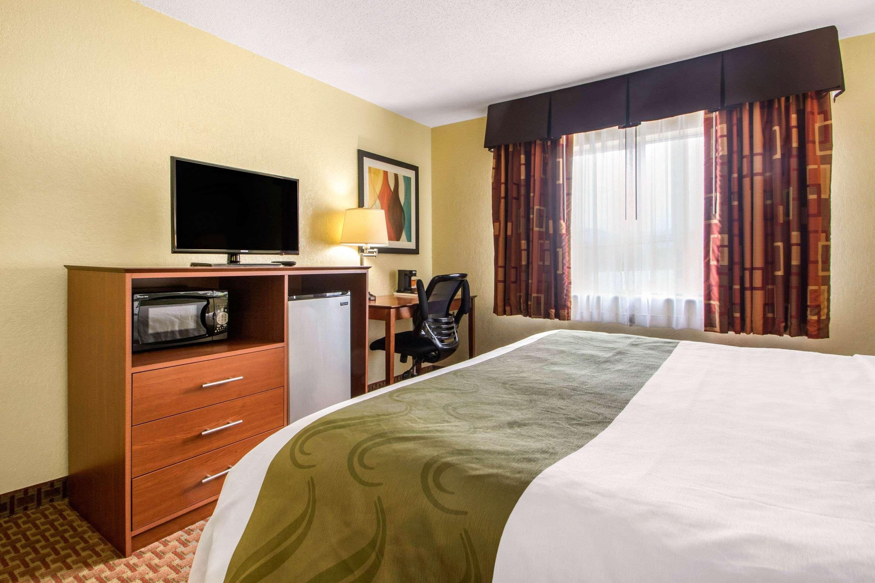 A hotel room with a bed, a desk with a computer, a television, and a microwave.