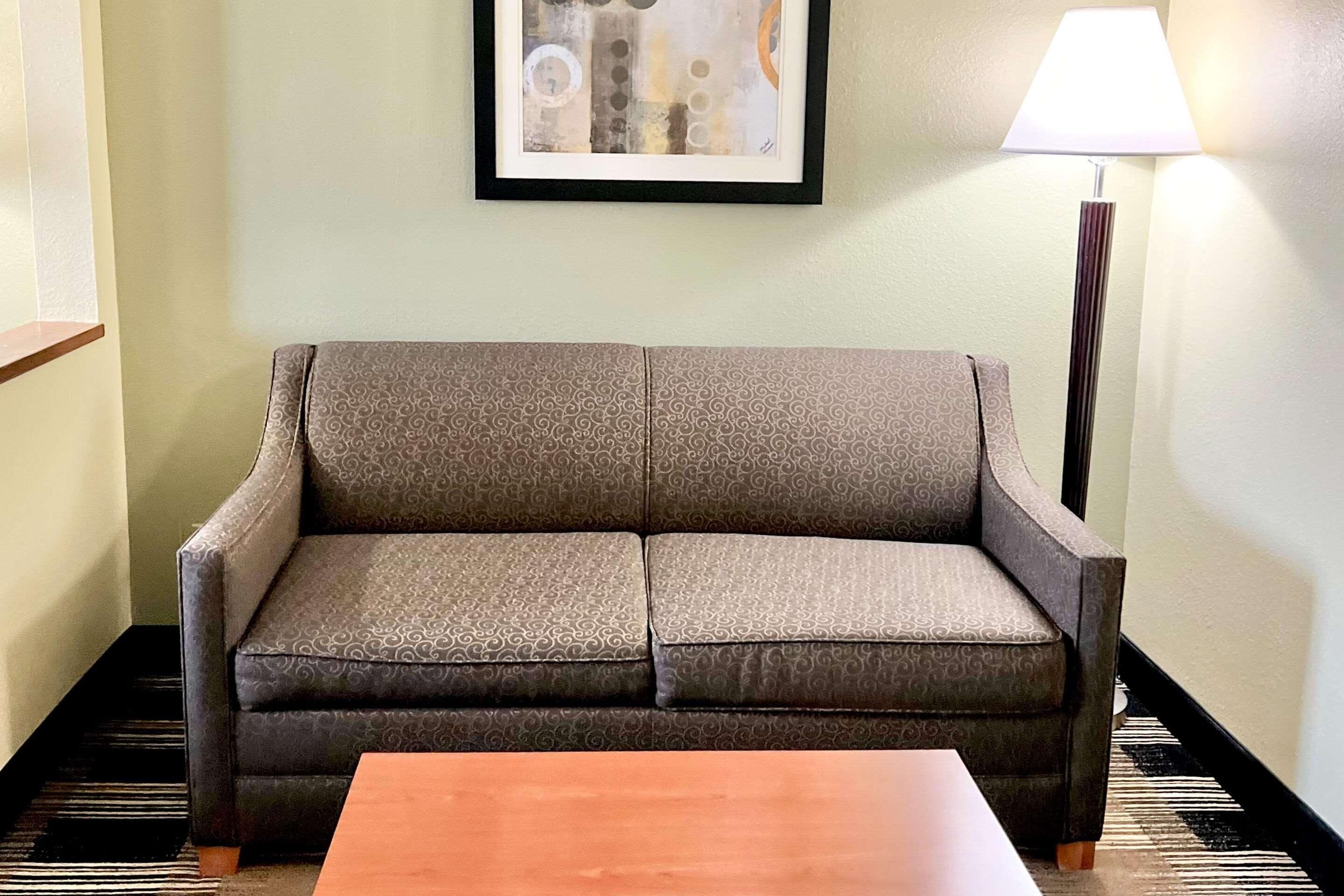 A sofa with a patterned fabric, a wooden coffee table, a framed abstract painting on the wall, and a floor lamp.