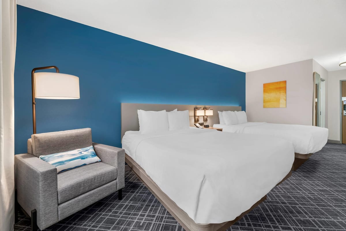 Quarto de hotel com uma cama grande, um sofá, uma mesa de cabeceira, um abajur e um quadro na parede.