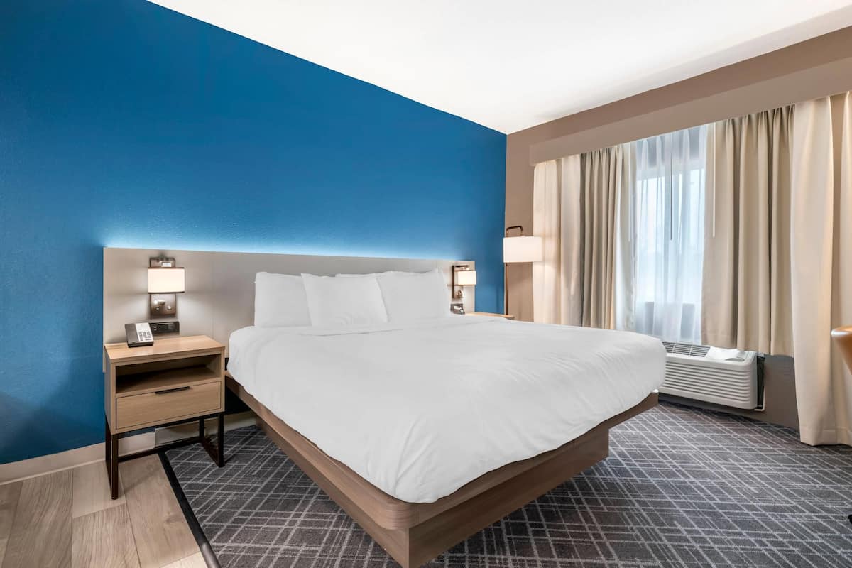 Quarto de hotel com uma cama grande, mesas de cabeceira com luminárias, uma janela com cortinas e um aparelho de ar condicionado.