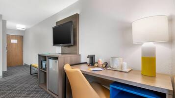A hotel room with a desk, chair, television, lamp, and a refrigerator.