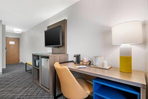 A hotel room with a desk, chair, television, lamp, and a refrigerator. - Quality Inn & SUI Wisconsin Dells Dwntn-waterparks (Wisconsin Dells)