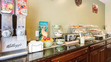 A breakfast buffet with various food items, a clock, and a fruit bowl.