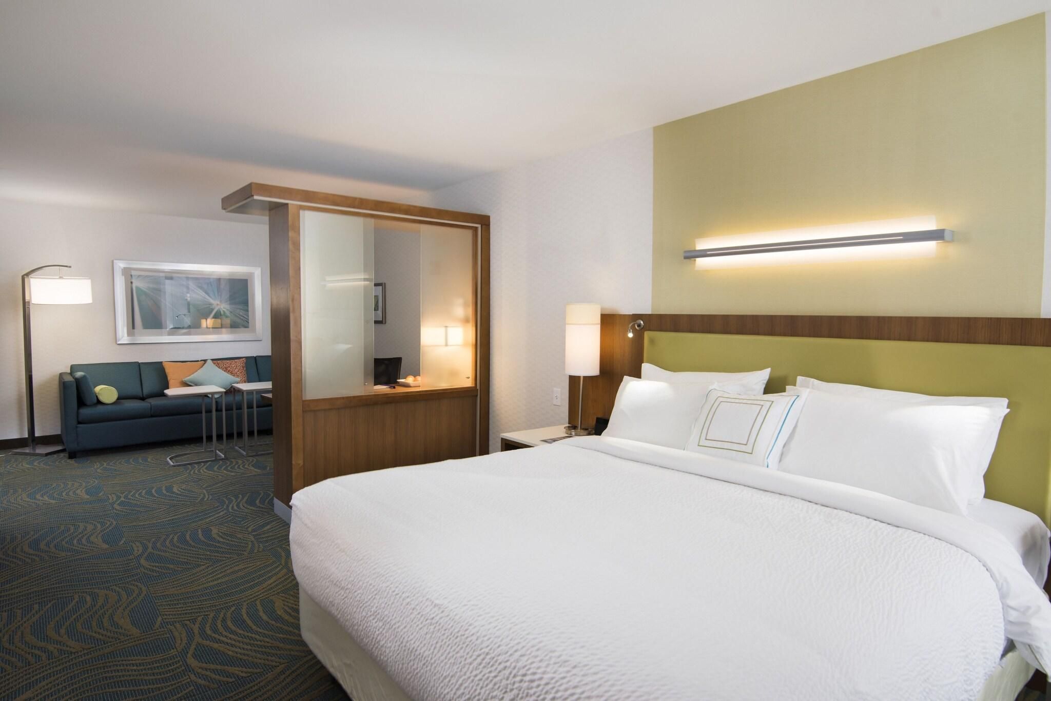 A hotel room with a large bed, a sofa, a desk, and a mirror.