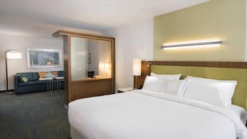 A hotel room with a large bed, a sofa, a desk, and a mirror.