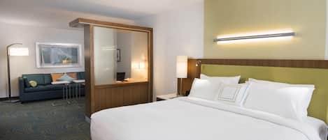 A hotel room with a large bed, a sofa, a desk, and a mirror.