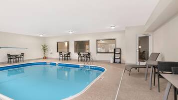 An indoor swimming pool with a tiled floor, surrounded by seating areas and windows.