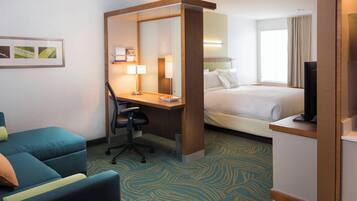 Ein Hotelzimmer mit Bett, Schreibtisch mit Stuhl, Fernseher und einer Couch.