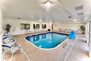 An indoor swimming pool with clear water, surrounded by white lounge chairs and a blue cover on one side. - Quality Inn & SUI Wisconsin Dells Dwntn-waterparks (Wisconsin Dells)