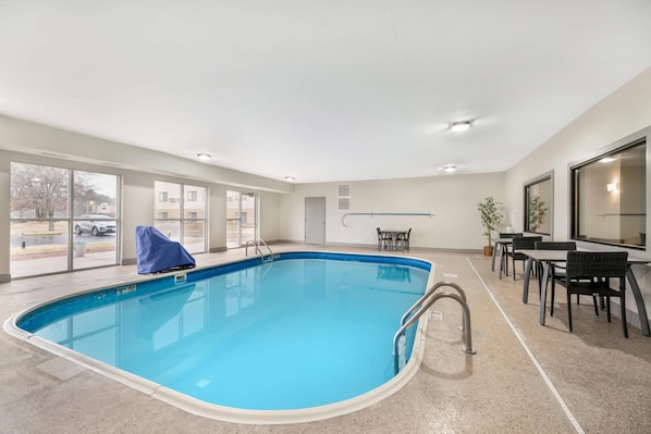 Piscina interna com vista desimpedida para o exterior, área coberta e espaço de estar com mesas e cadeiras.