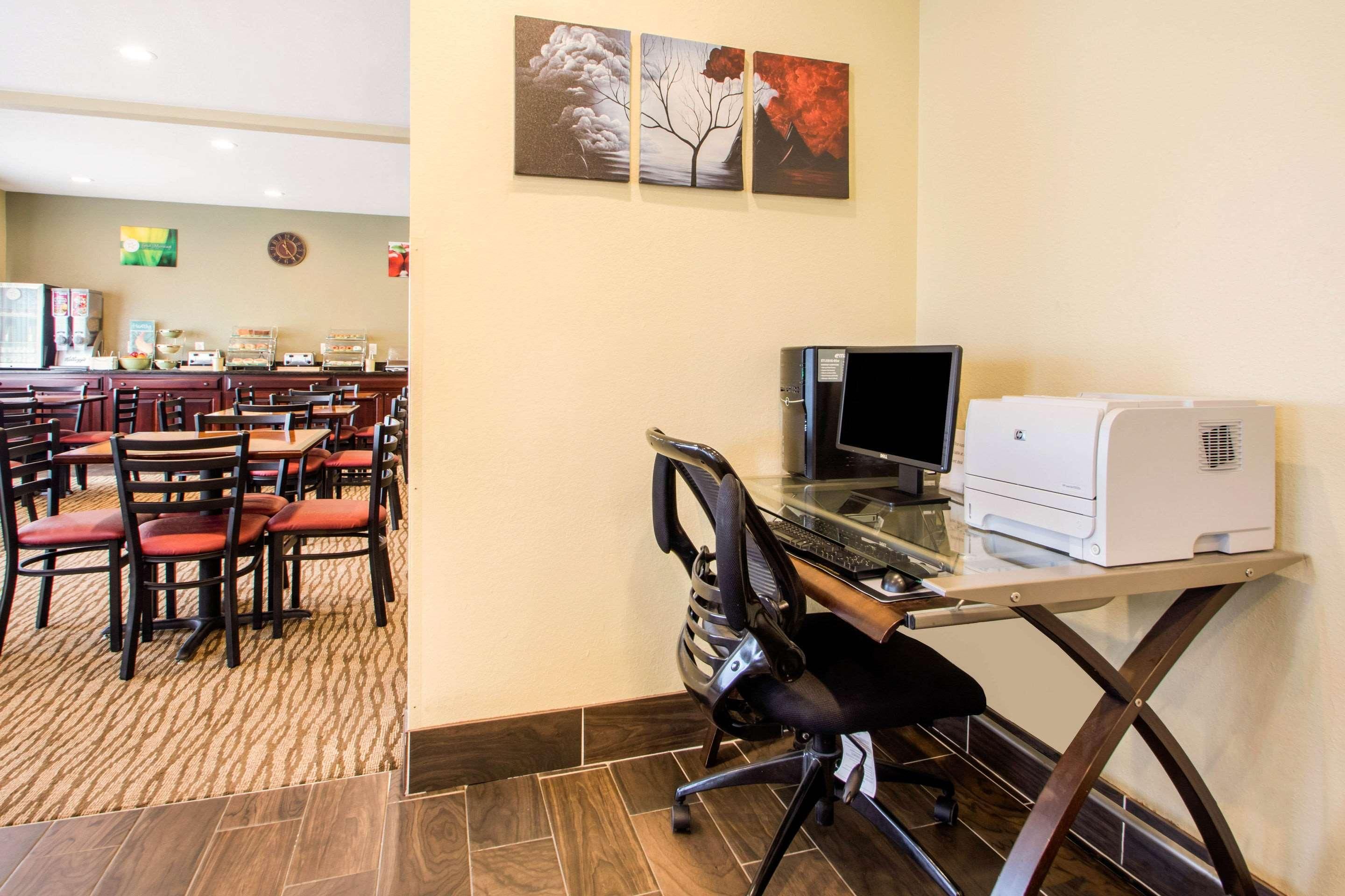 A hotel room with a dining area, a desk with a computer and printer, and artwork on the wall.