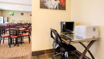 A hotel room with a dining area, a desk with a computer and printer, and artwork on the wall.