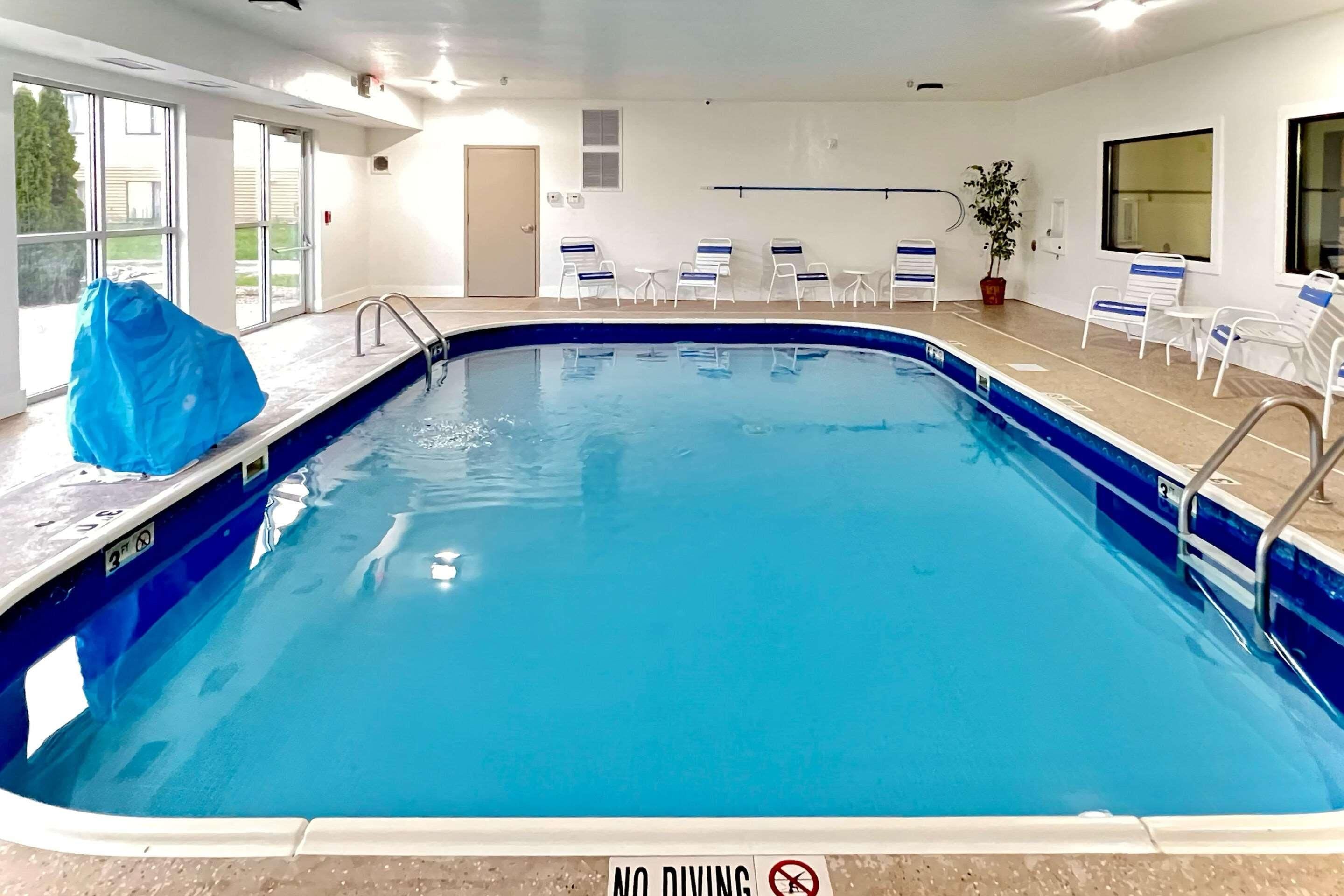 An indoor swimming pool with a 'NO DIVING' sign, lounge chairs, and a potted plant.