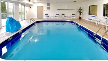 An indoor swimming pool with a 'NO DIVING' sign, lounge chairs, and a potted plant.