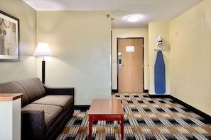 Habitación de hotel con sofá, una mesita, lámpara, puerta y alfombra estampada.