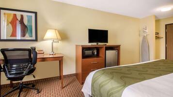 A hotel room with a bed, desk, chair, television, microwave, and ironing board.