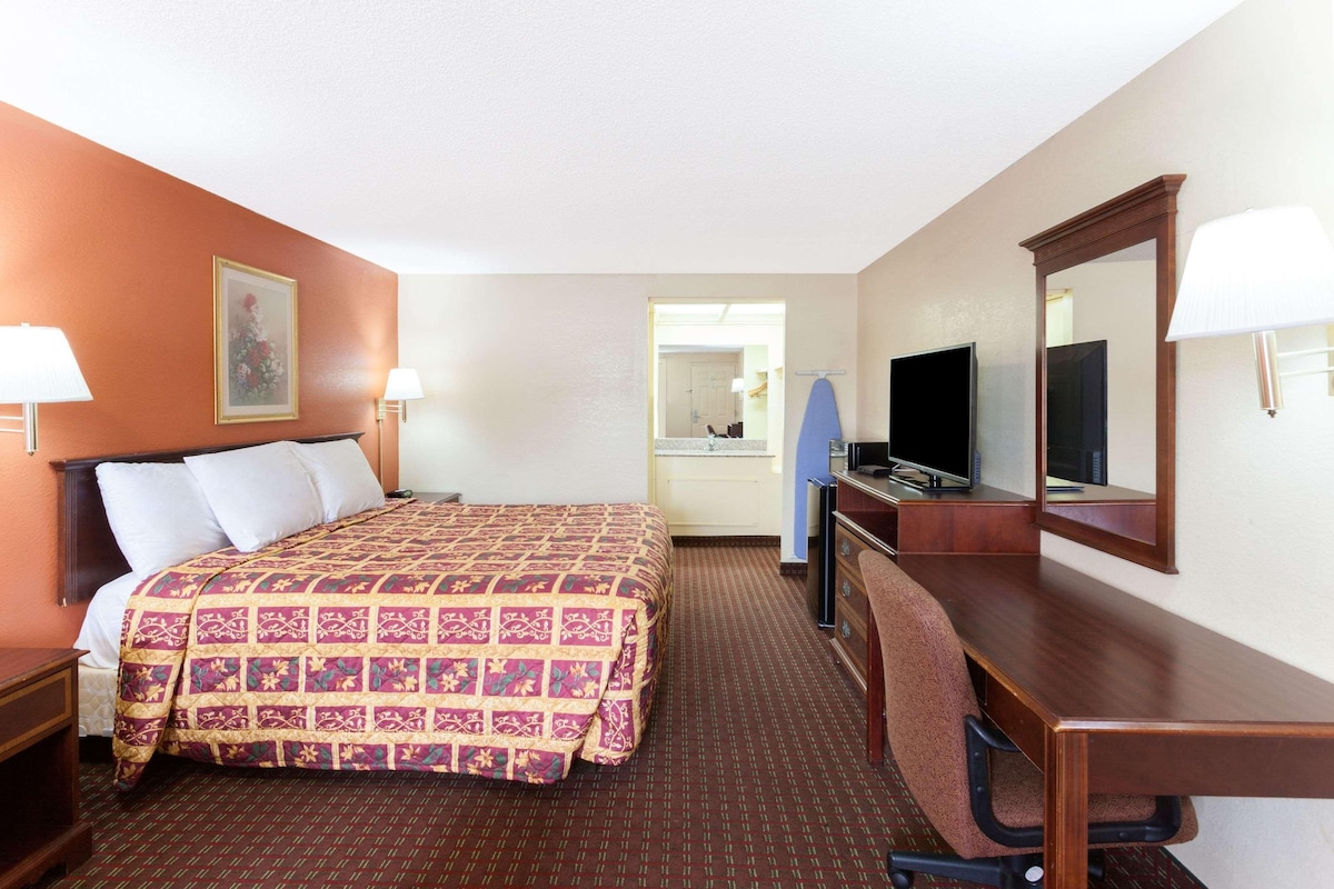 A hotel room with a bed, desk, chair, television, and a mirror.