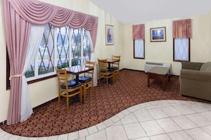 A room with a dining table, chairs, a sofa, a radiator, and a window with curtains. - Knights Inn Tucker (Atlanta)
