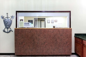 A reception desk with a marble top, a coat of arms on the wall, and various notices and signs. - Knights Inn Tucker (Atlanta)