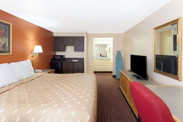 A hotel room with a bed, a desk with a TV, a mirror, a kitchenette, and a bathroom visible through an open door. - Knights Inn Tucker (Atlanta)